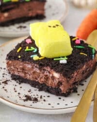 A slice of Easter dirt cake topped with a yellow marshmallow Peep bunny on a plate.