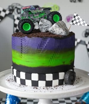 A Gravedigger monster truck cake on a white cake stand.