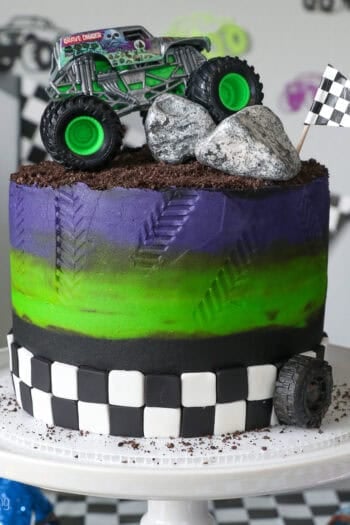 A Gravedigger monster truck cake on a white cake stand.