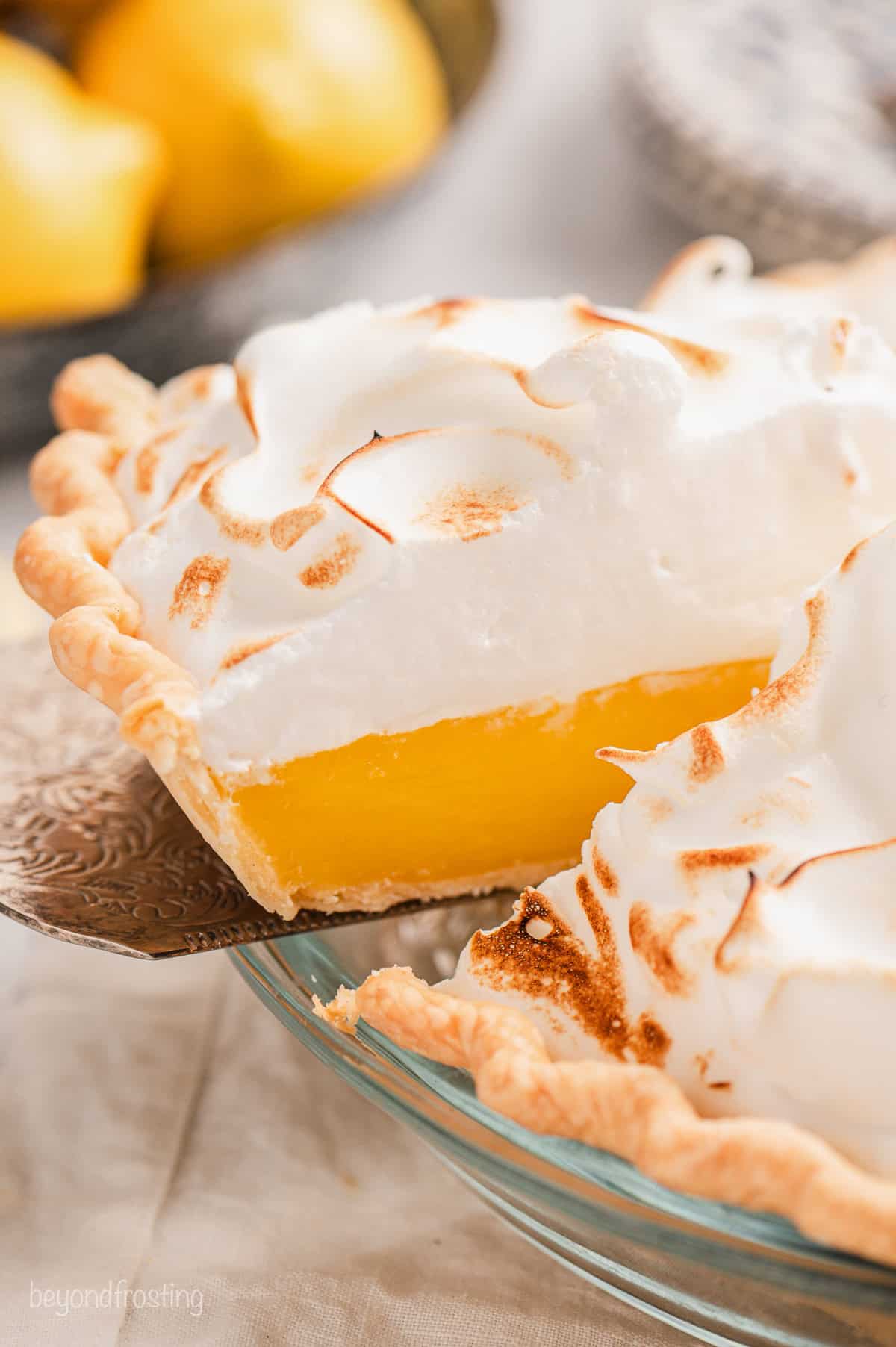 A slice of lemon meringue pie partially lifted from the rest of the pie with a cake server.