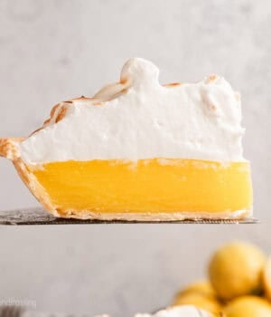 A slice of lemon meringue pie held above the rest of the pie with a cake server.