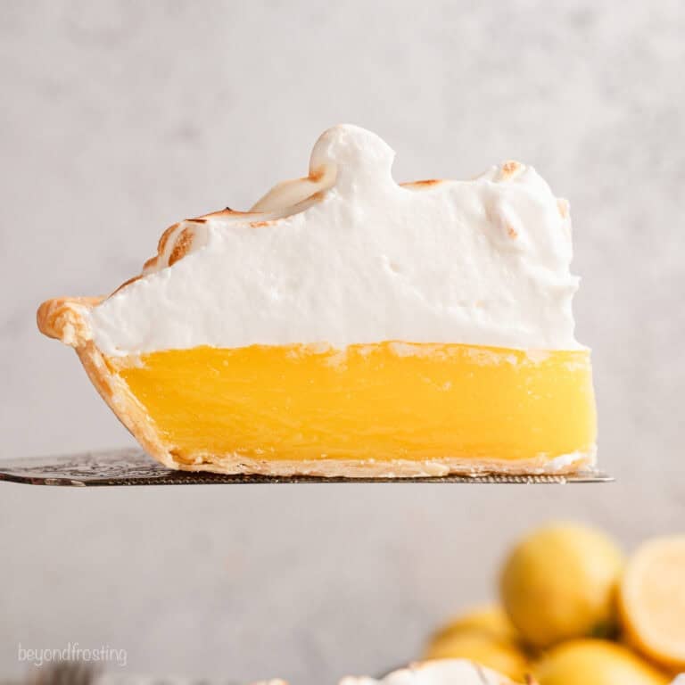 A slice of lemon meringue pie held above the rest of the pie with a cake server.