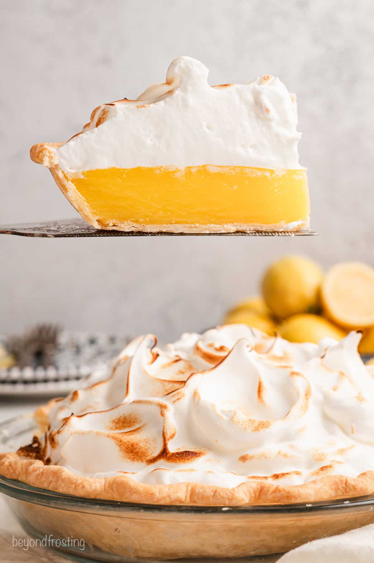 This homemade lemon meringue pie has a buttery crust and sweet-tart lemon curd topped with mile-high peaks of toasted marshmallowy meringue! A slice of lemon meringue pie held above the rest of the pie with a cake server.
