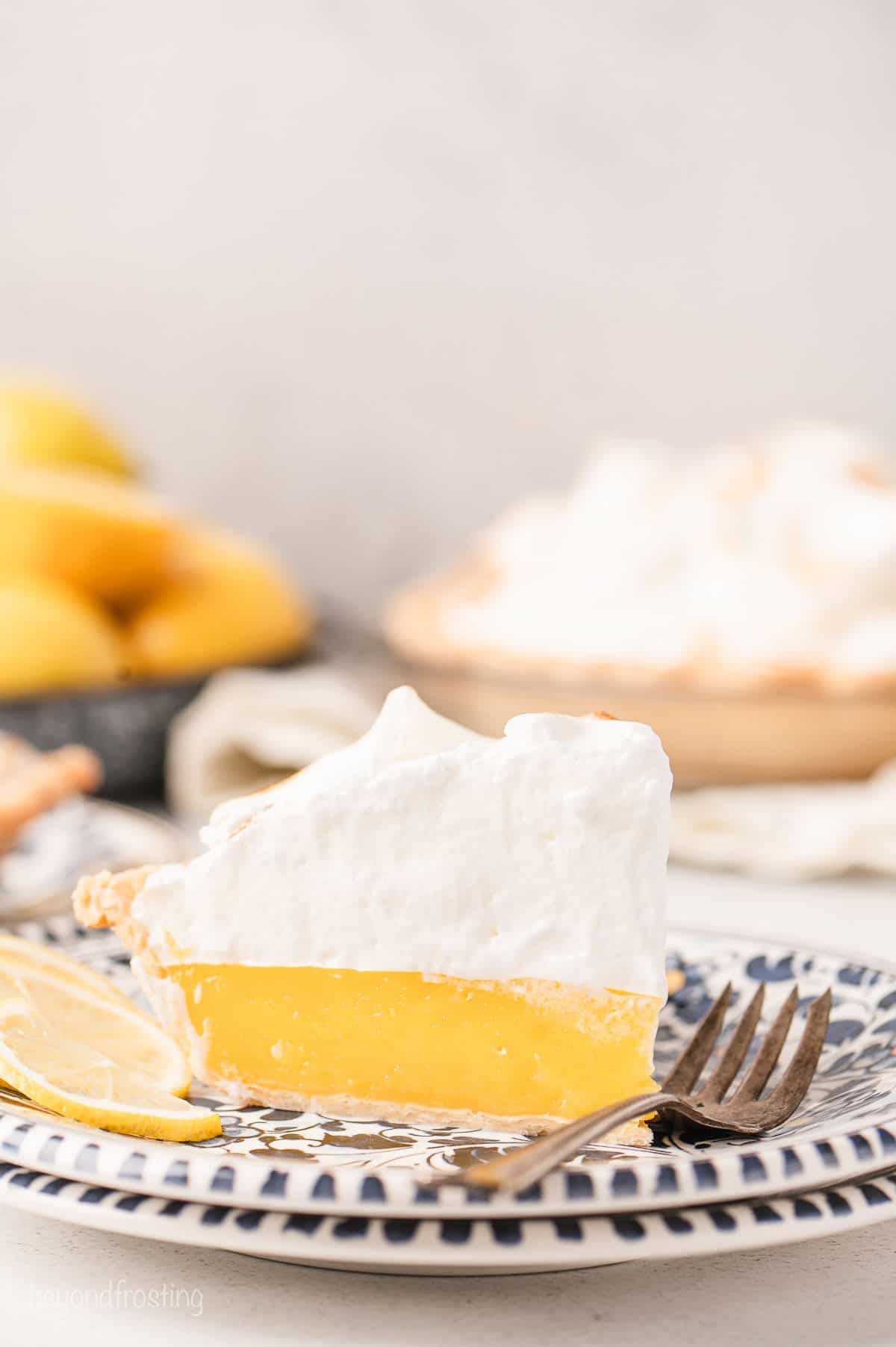 A slice of lemon meringue pie on a plate next to a fork.