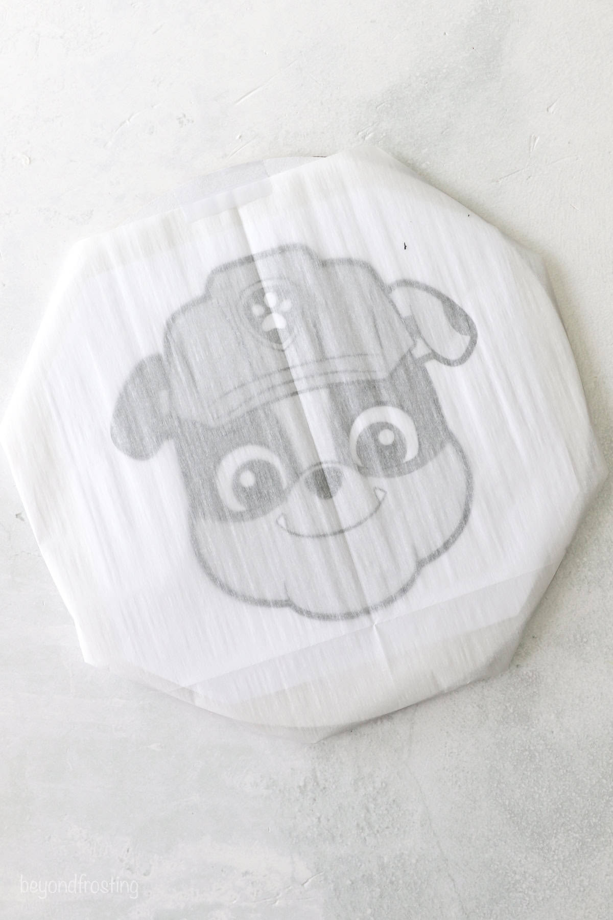 A round cardboard cake plate with stencil under a piece of parchment paper.