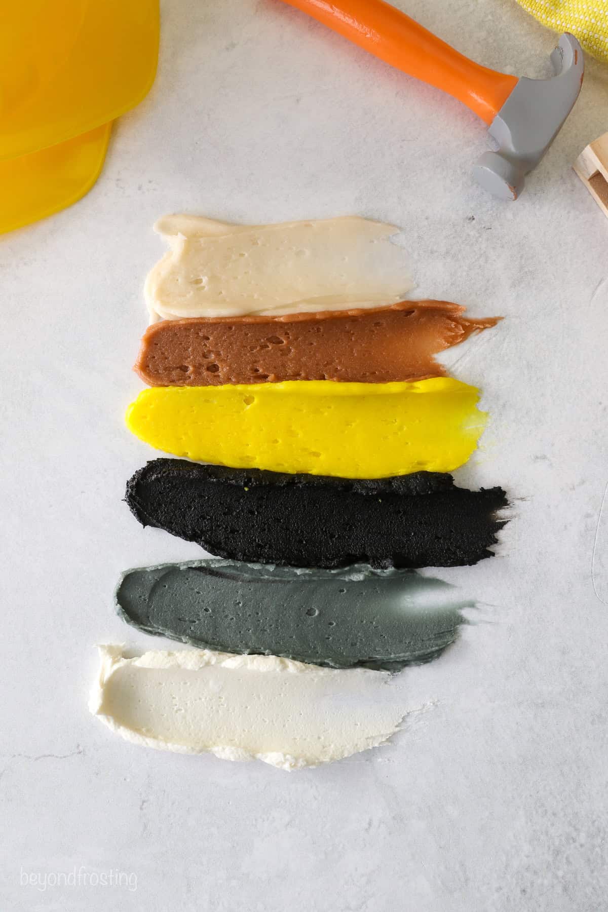 Smudged buttercream swatches on a countertop showing each color: tan, brown, yellow, black, gray, and white.