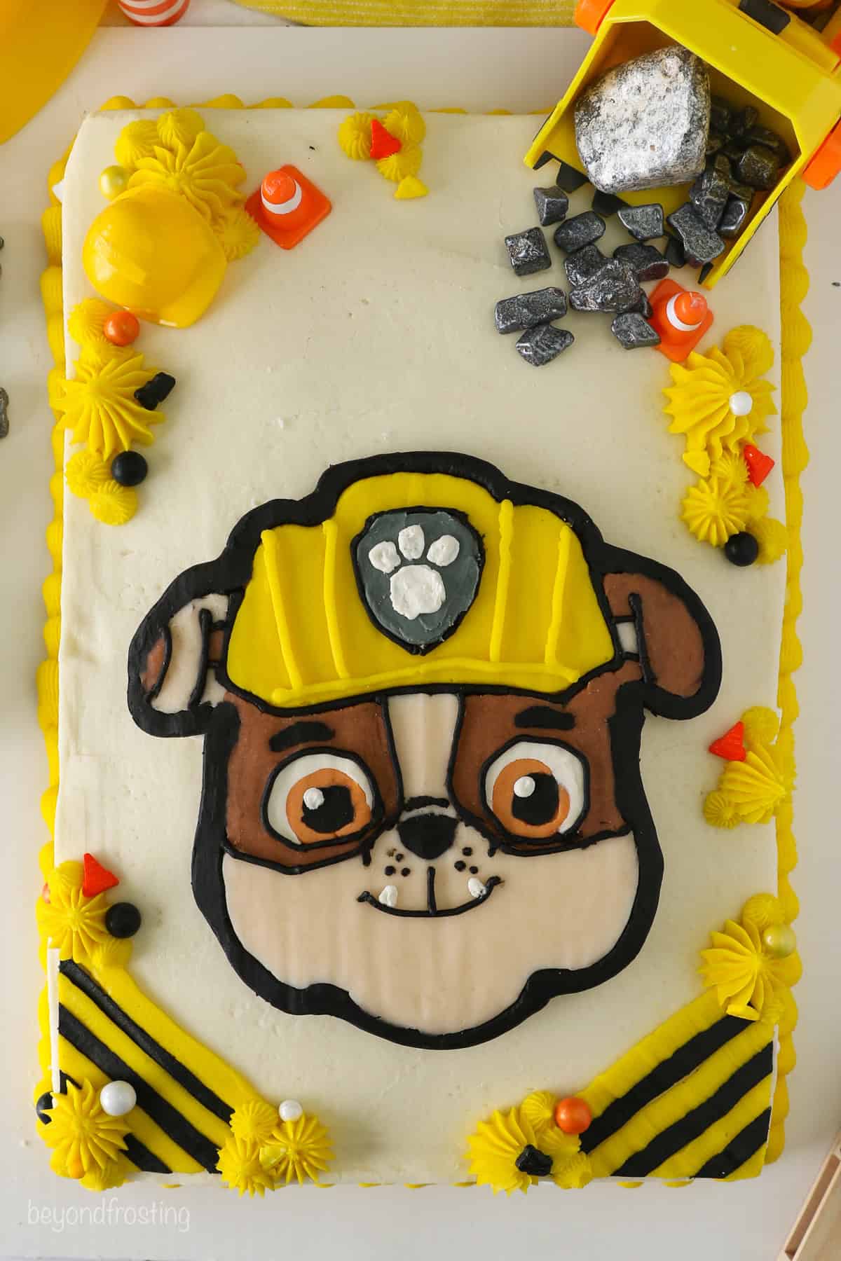 Overhead view of a Rubble Paw Patrol Cake with Rubble's detailed face in the center, surrounded by piped buttercream shells and construction decorations.