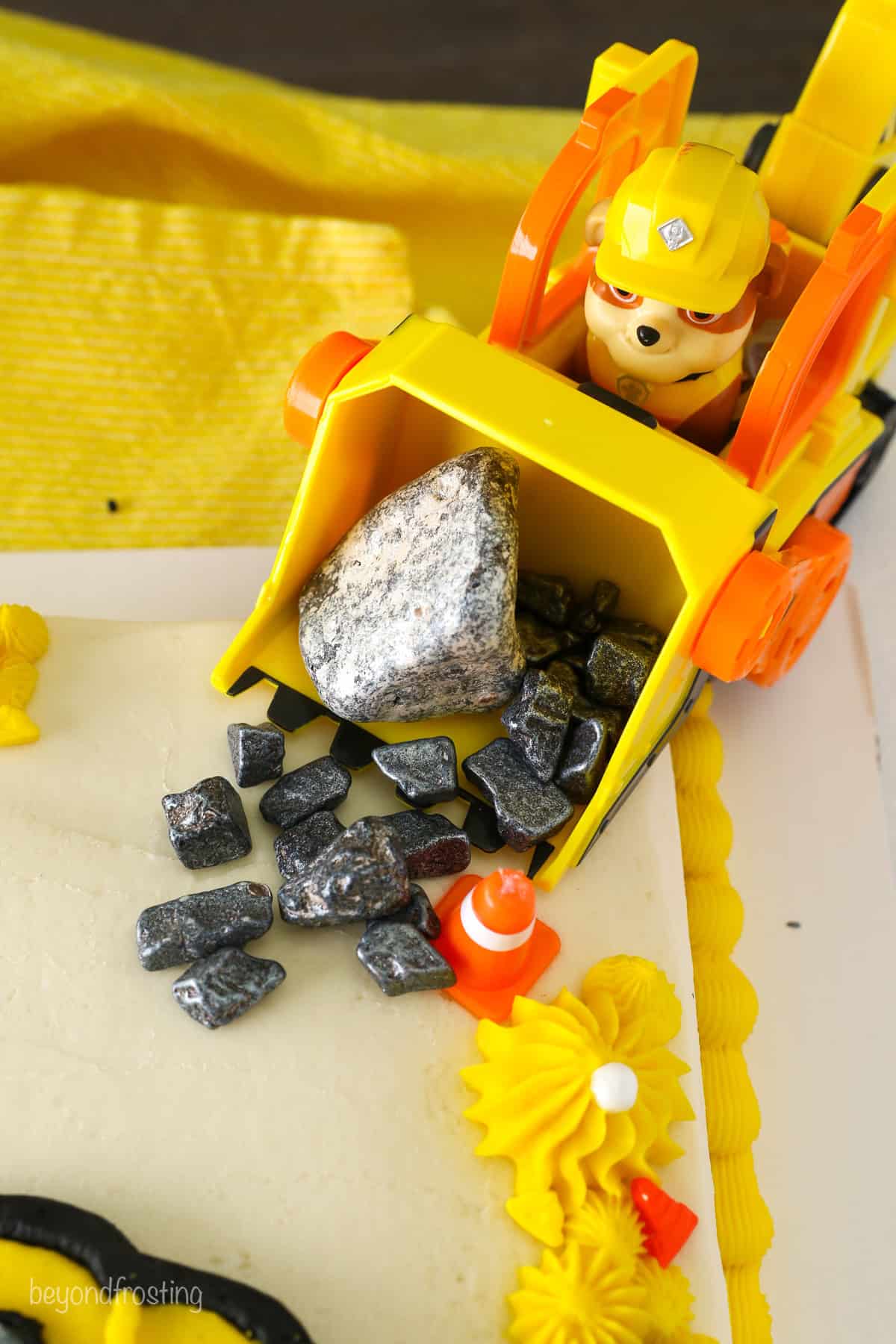 Close up of a small excavator figurine dumping decorative rocks at the corner of a Paw Patrol cake.