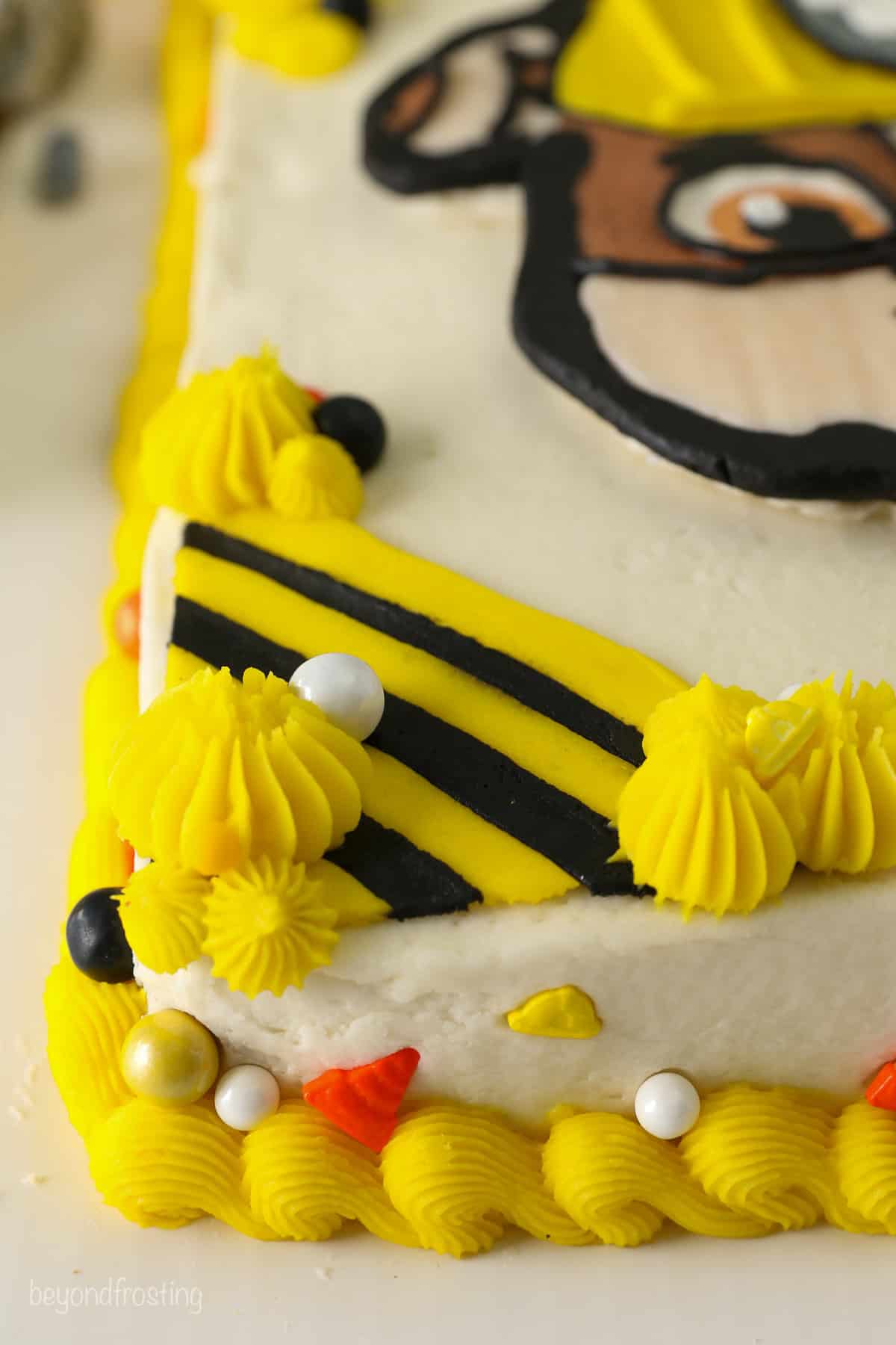 Close up of yellow and black piped construction stripes in the corner of a Paw Patrol cake, decorated with yellow buttercream shells.