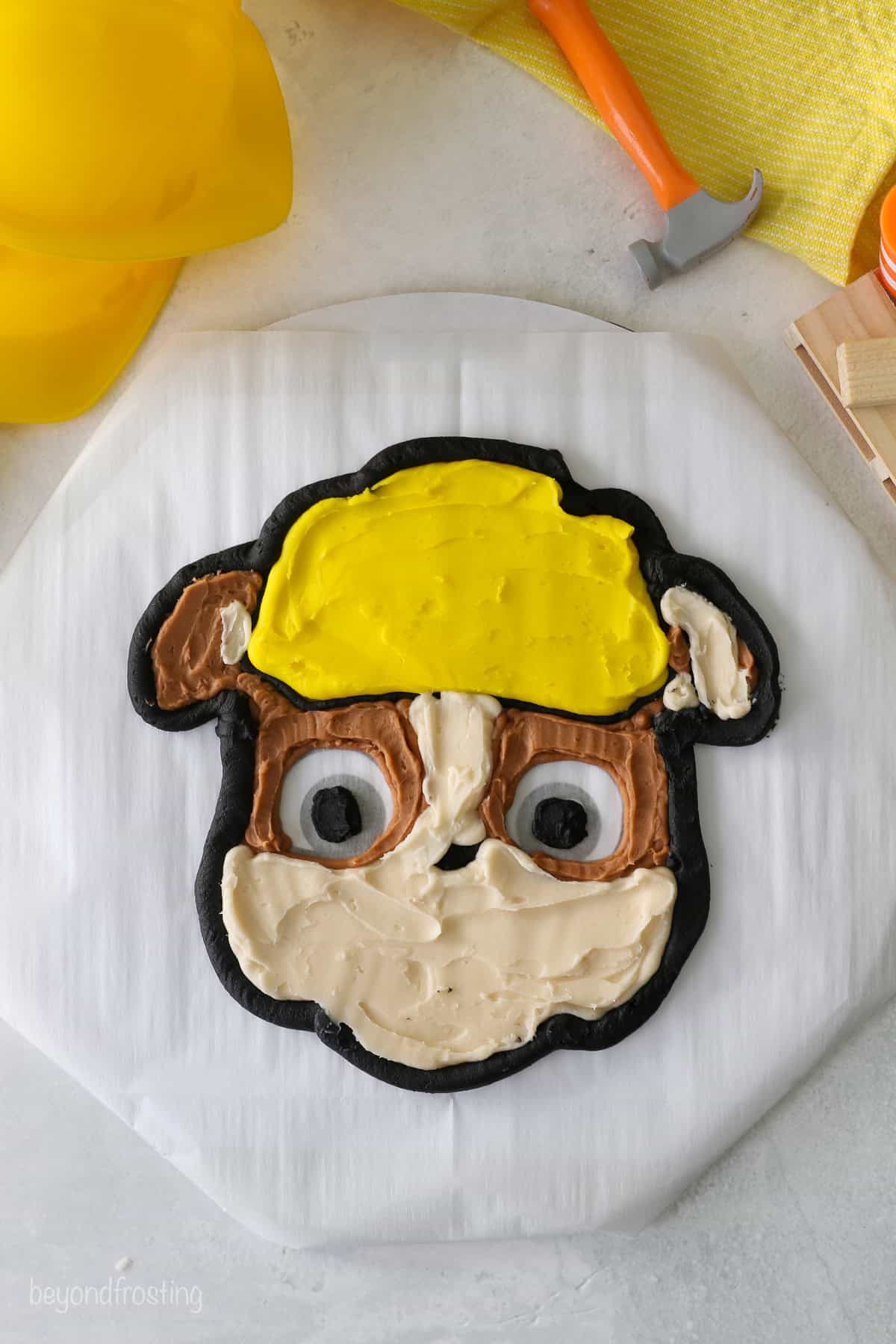 Rubble's piped black buttercream outline partially filled in with yellow, brown, and tan buttercream on a piece of parchment paper.