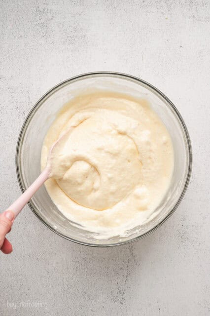 Vanilla cake batter being stirred with a spatula in a glass bowl.