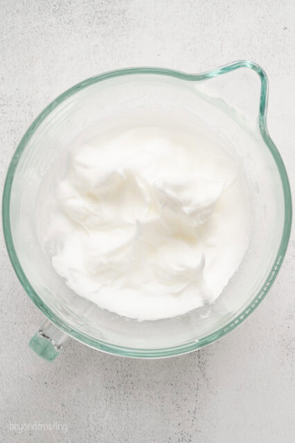 Whipped egg whites in a glass mixing bowl.