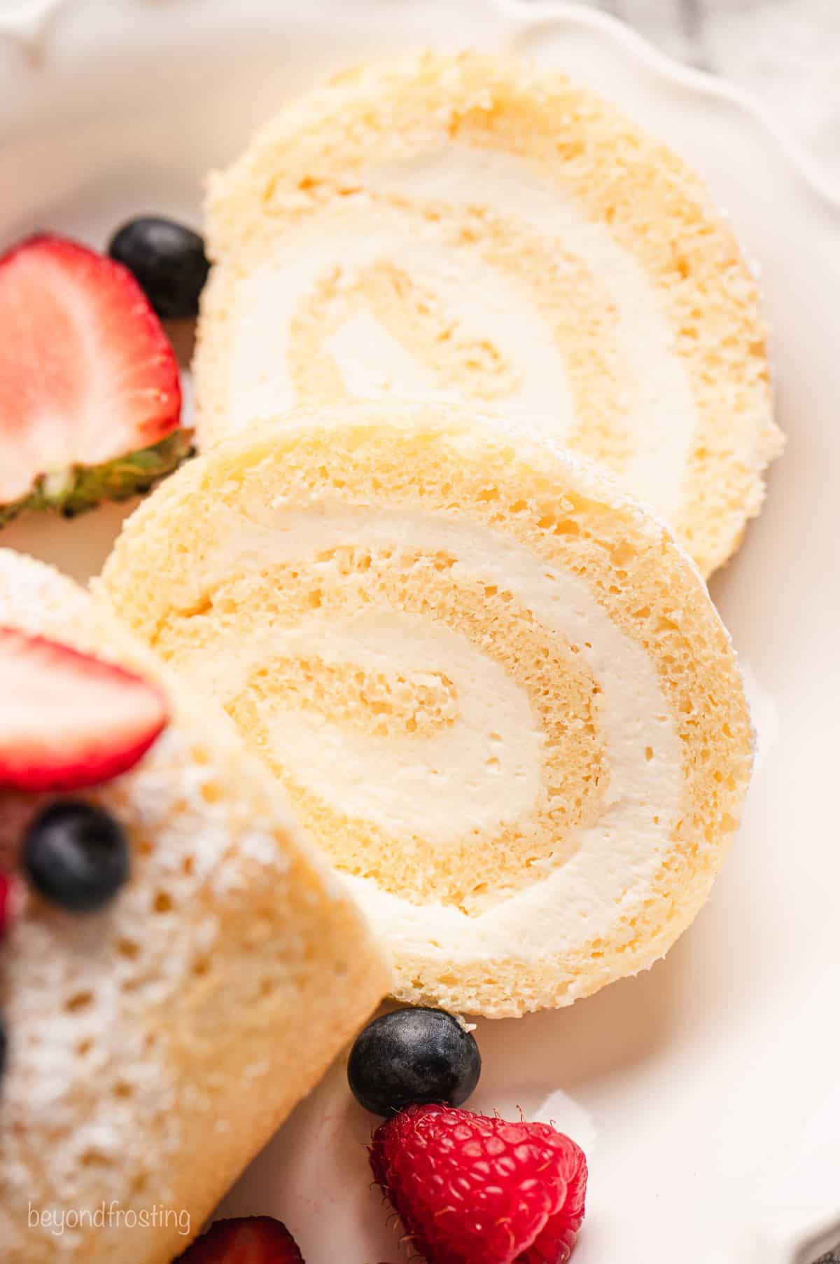 Close up of two slices cut from the end of a vanilla cake roll topped with fresh berries.