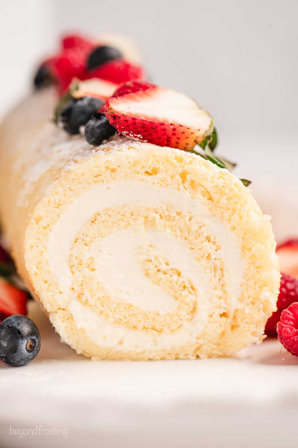 Close up front view of a vanilla cake roll topped with fresh mixed berries.