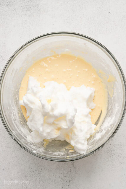 Whipped egg whites added to cake batter in a glass bowl.