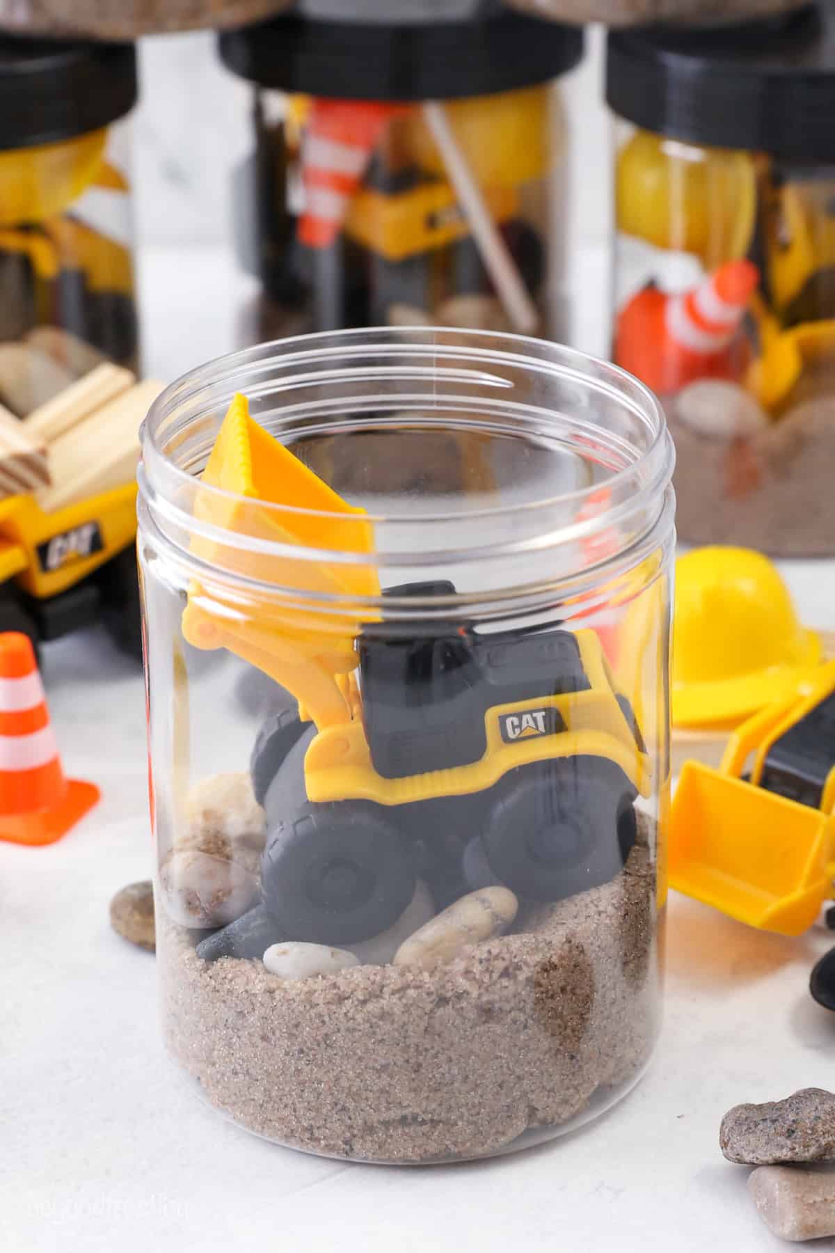 Kinetic sand and a toy digger inside an open jar.