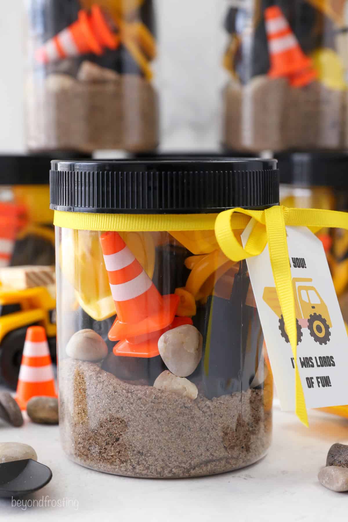 A jar filled with kinetic sand and construction party favors with a gift tag attached.