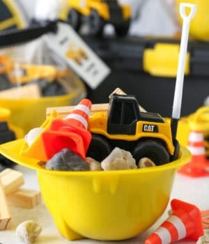 A yellow construction hat bowl filled with construction-themed party favors on a tabletop surrounded by more party decorations.