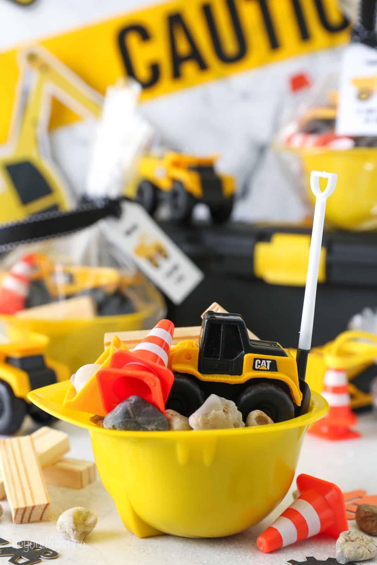 An easy tutorial for fun, DIY construction party favors for kids! These are perfect for a little digger’s construction themed birthday party. A yellow construction hat bowl filled with construction-themed party favors on a tabletop surrounded by more party decorations.