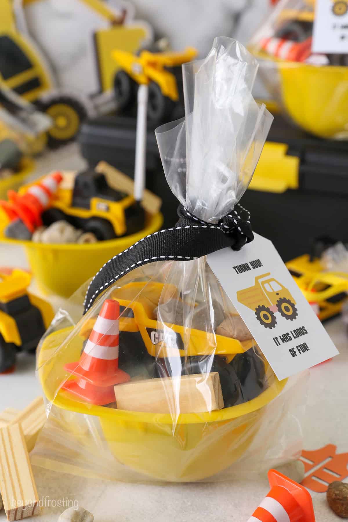 A yellow construction hat bowl filled with construction-themed party favors wrapped in cellophane on a tabletop surrounded by more party decorations.