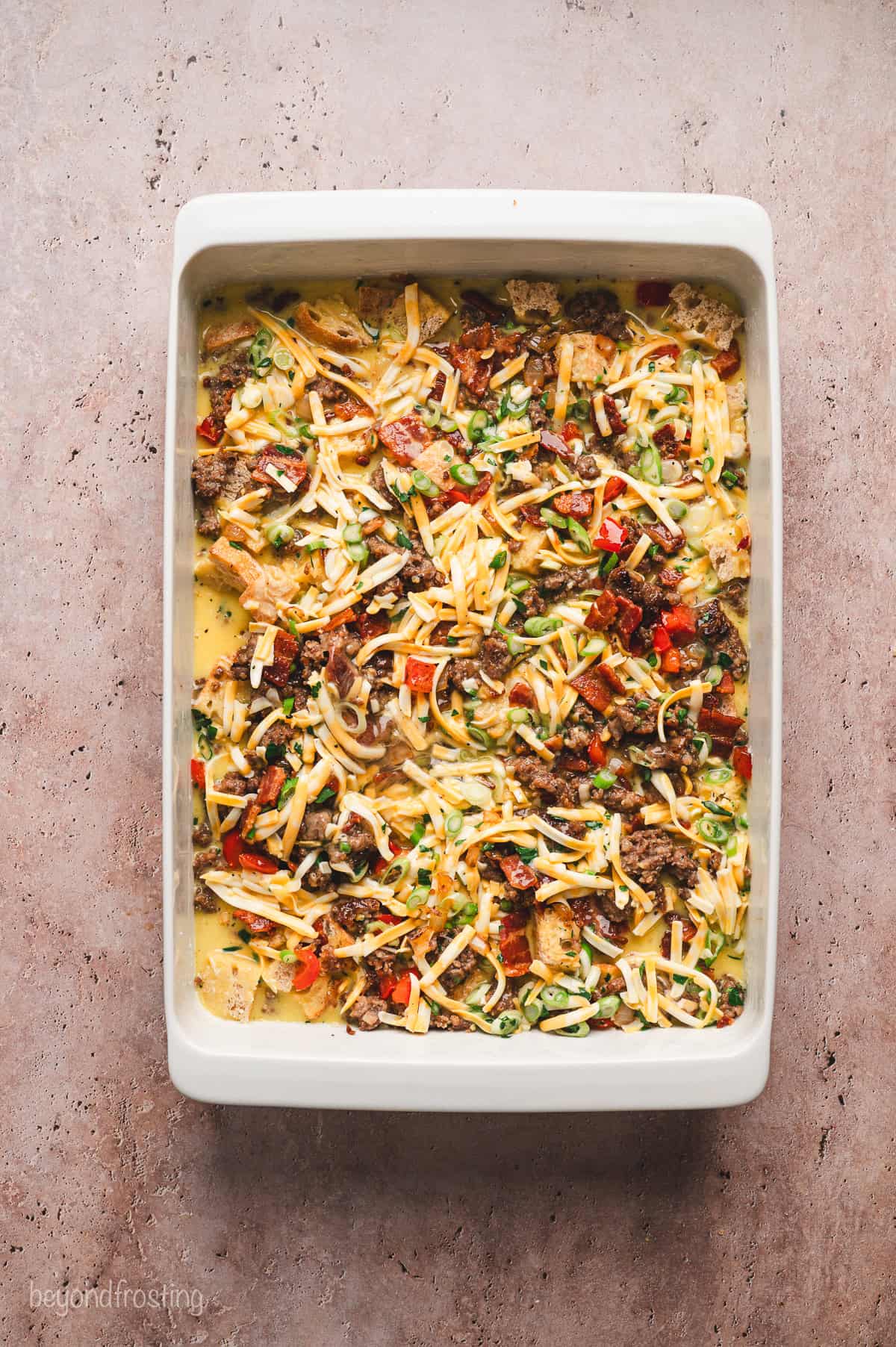 Overhead view of an assembled breakfast egg casserole topped with cheese in a baking dish.