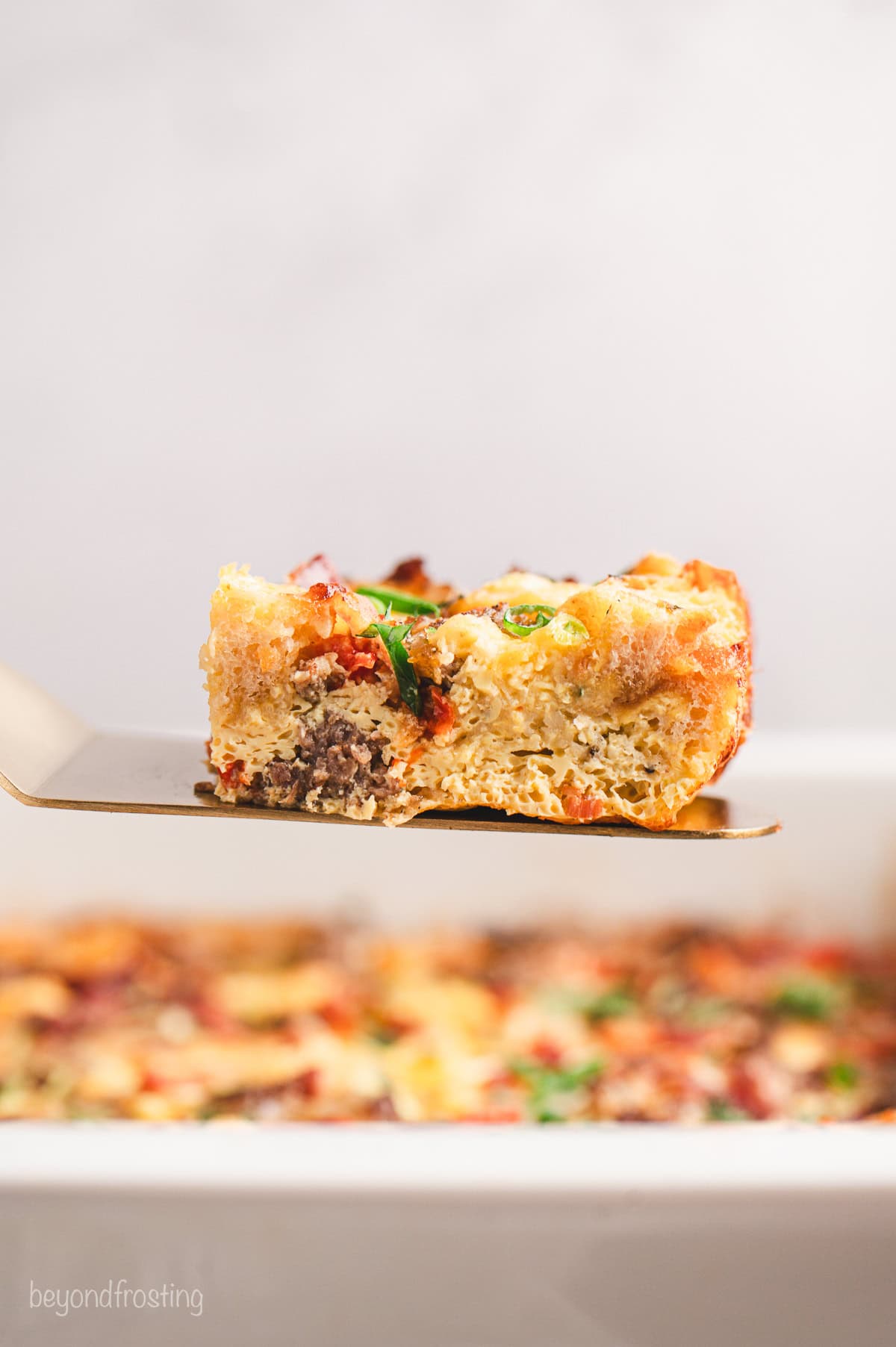 Side view of a slice of breakfast casserole being lifted from the rest of the casserole in a baking dish.