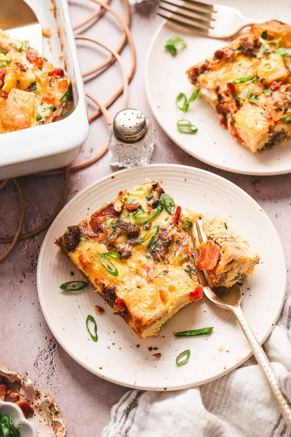 Slices of breakfast egg casserole served on two plates with forks.