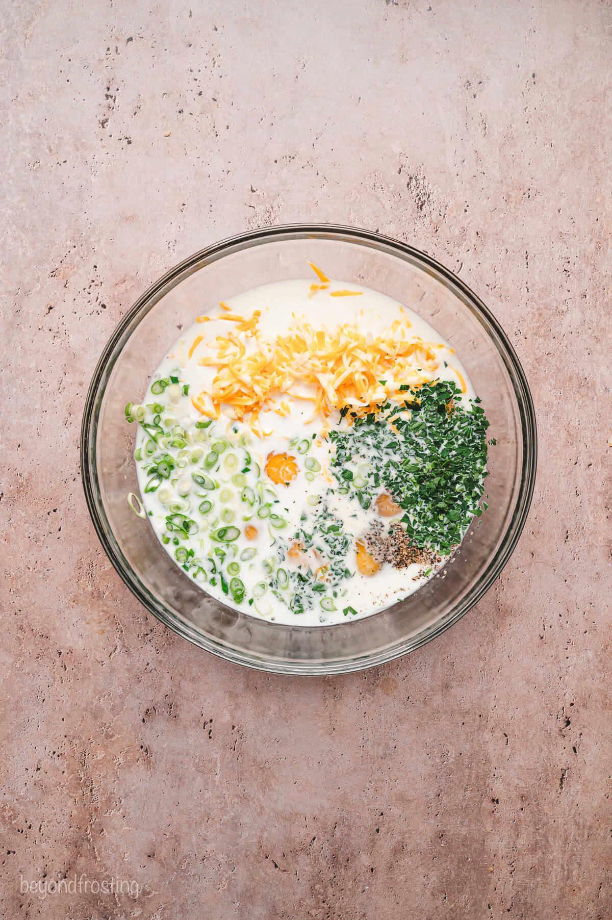 Eggs, milk, and fresh herbs combined in a bowl.