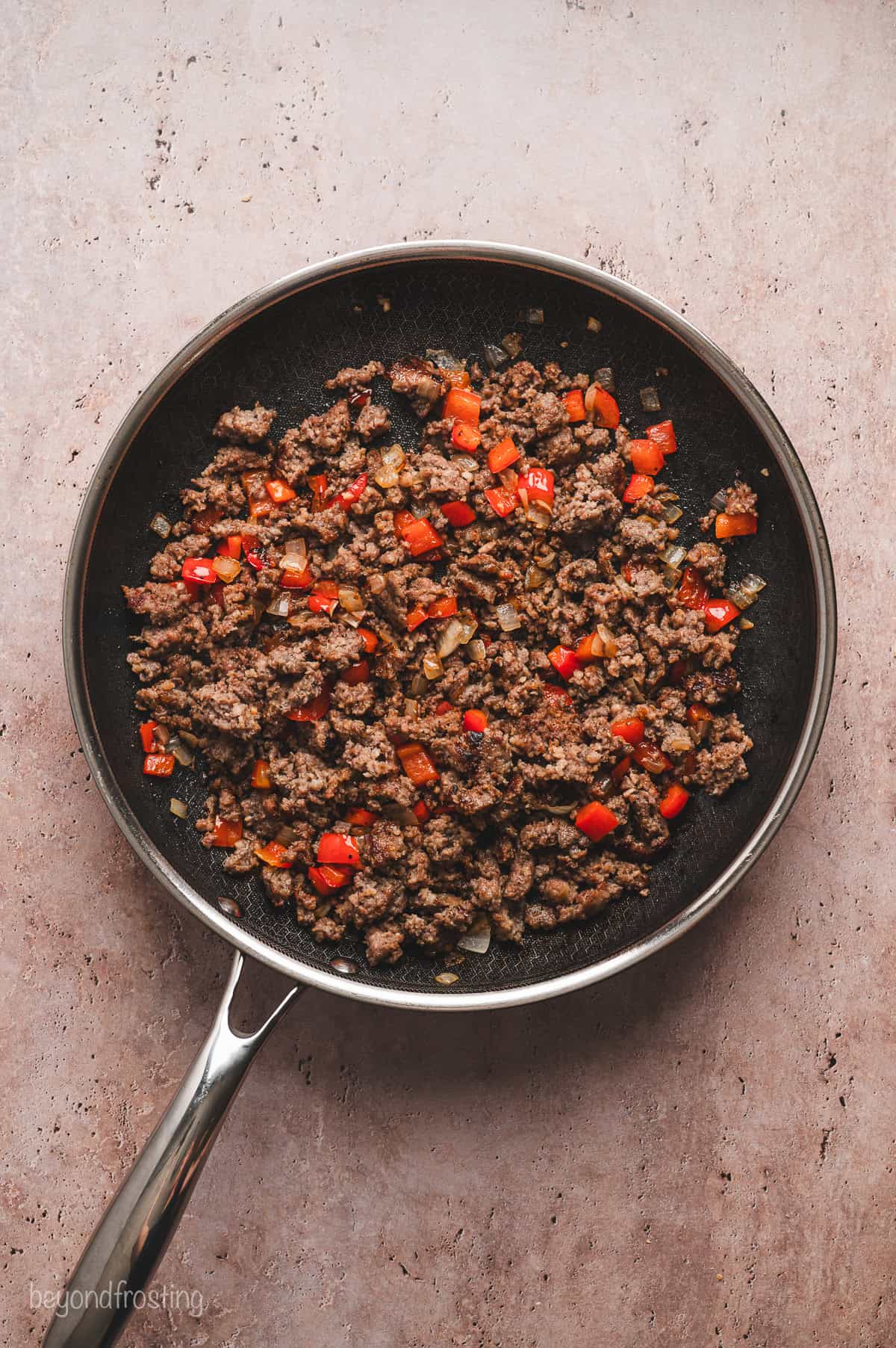 Browned sausage with sautéed red peppers and onions in a skillet.