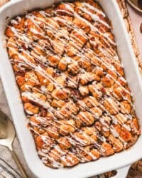 Overhead view of a cinnamon roll casserole drizzled with cream cheese icing in a baking dish.