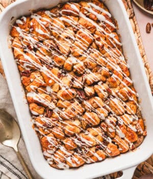 Overhead view of a cinnamon roll casserole drizzled with cream cheese icing in a baking dish.