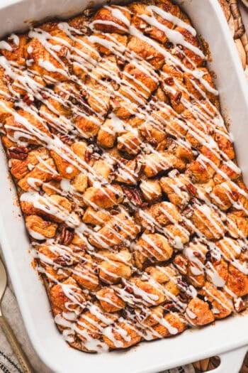 Overhead view of a cinnamon roll casserole drizzled with cream cheese icing in a baking dish.