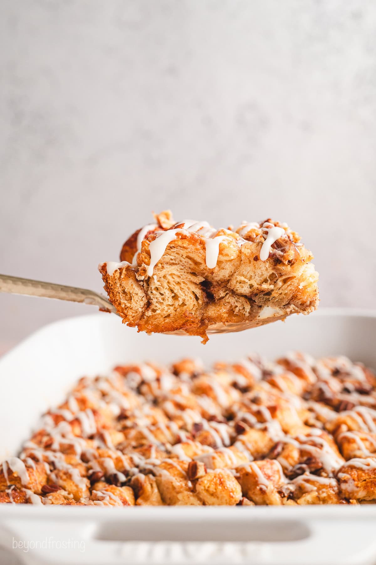 Side view of a slice of cinnamon roll casserole being lifted from the rest of the casserole in a baking dish.