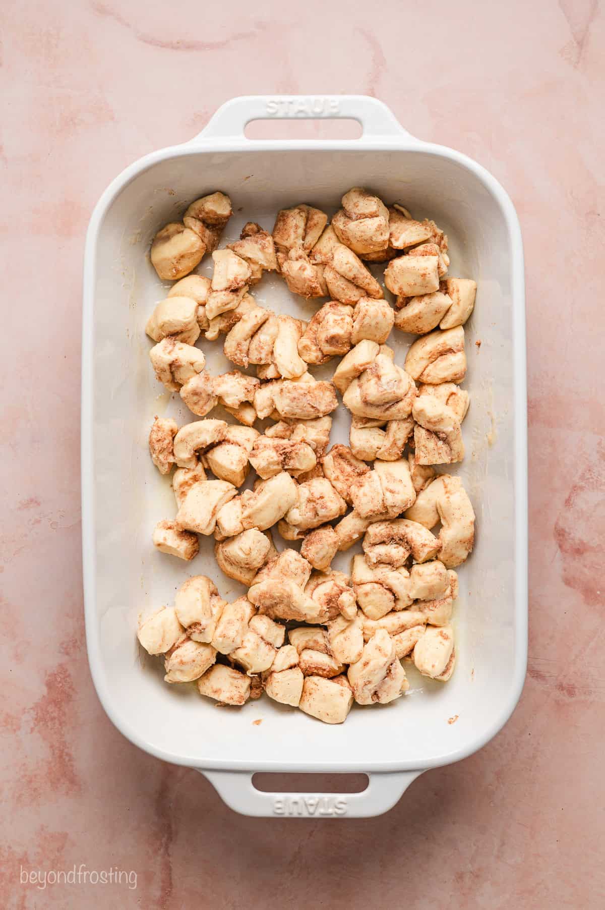 Refrigerated cinnamon roll pieces added to a baking dish.