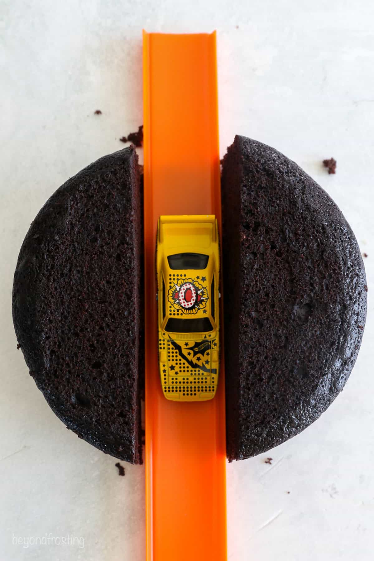 Overhead view of a Hot Wheels track with a toy car set down the middle of two halves of a cake layer.