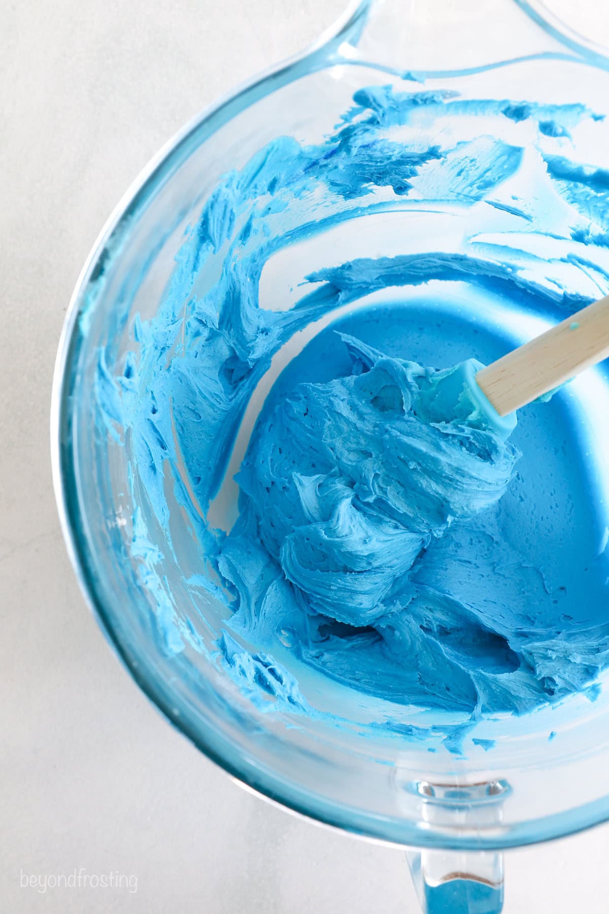 Vanilla buttercream colored blue in a white bowl with a spatula.