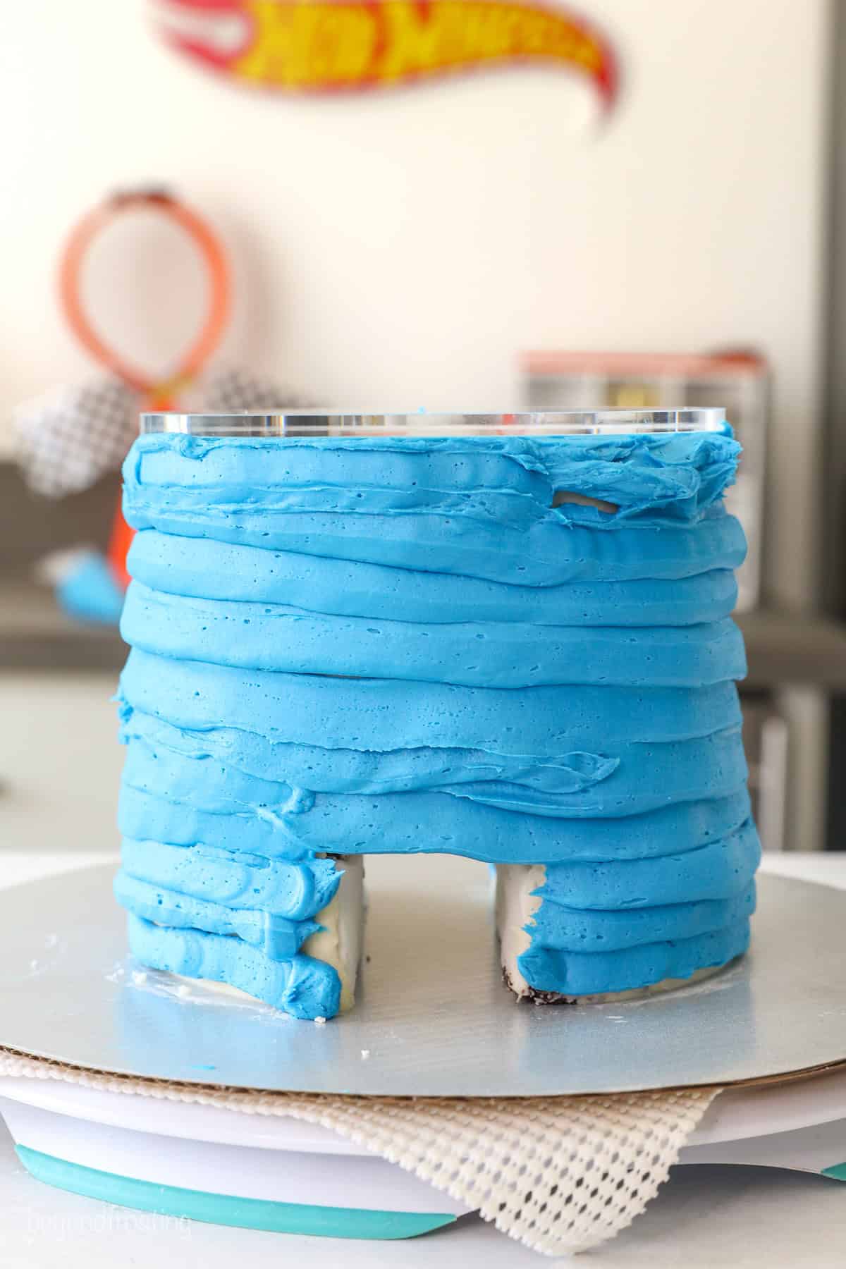 Side view of a layer cake covered with piped blue buttercream with a hole cut through the bottom of the cake, creating a tunnel.