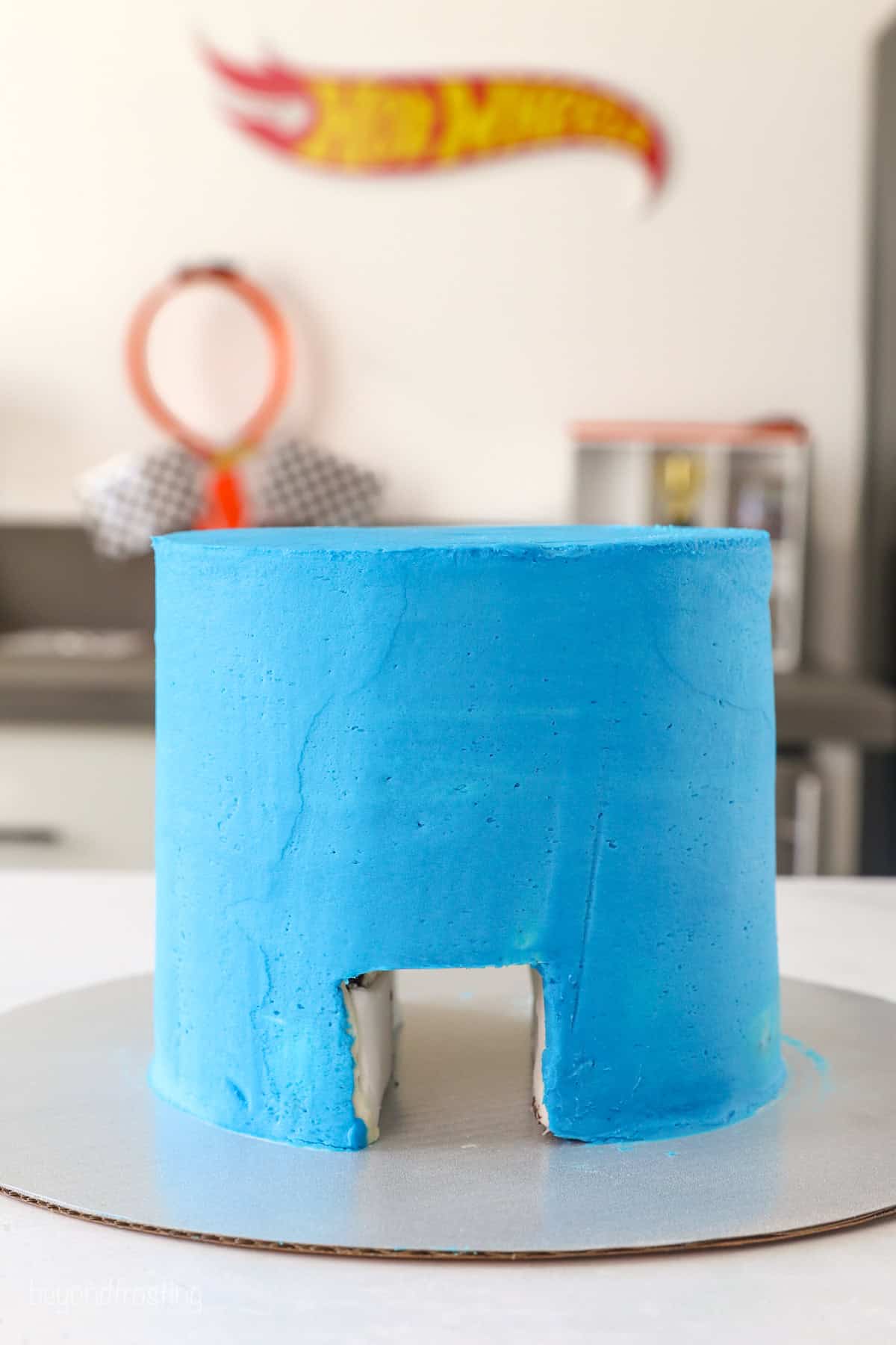 Side view of a layer cake frosted with blue buttercream with a hole cut through the bottom of the cake, creating a tunnel.