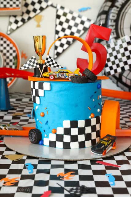A Hot Wheels cake topped with a loop and a mini trophy, decorated with blue frosting and checkered fondant.