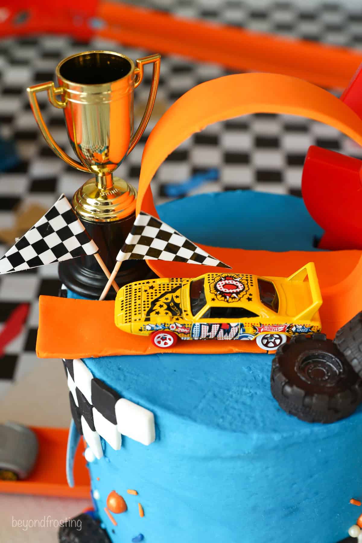 Overhead close up view of a Hot Wheels cake topped with a toy car, a fondant loop, and a min i trophy with chocolate tires.