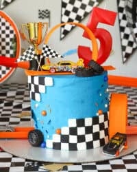A Hot Wheels cake topped with a loop and a mini trophy, decorated with blue frosting and checkered fondant.