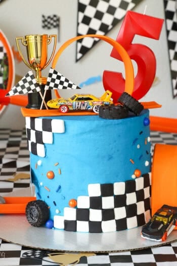 A Hot Wheels cake topped with a loop and a mini trophy, decorated with blue frosting and checkered fondant.