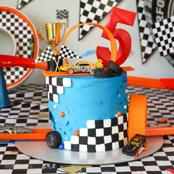 A Hot Wheels cake topped with a loop and a mini trophy, decorated with blue frosting and checkered fondant.
