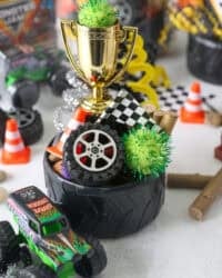 A tire bowl filled with Monster truck party favors, including mini tires, pompoms, a mini checkered flag, and a toy trophy.