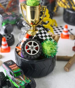 A tire bowl filled with Monster truck party favors, including mini tires, pompoms, a mini checkered flag, and a toy trophy.