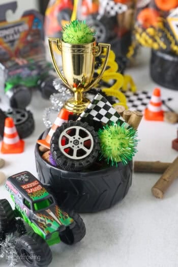 A tire bowl filled with Monster truck party favors, including mini tires, pompoms, a mini checkered flag, and a toy trophy.