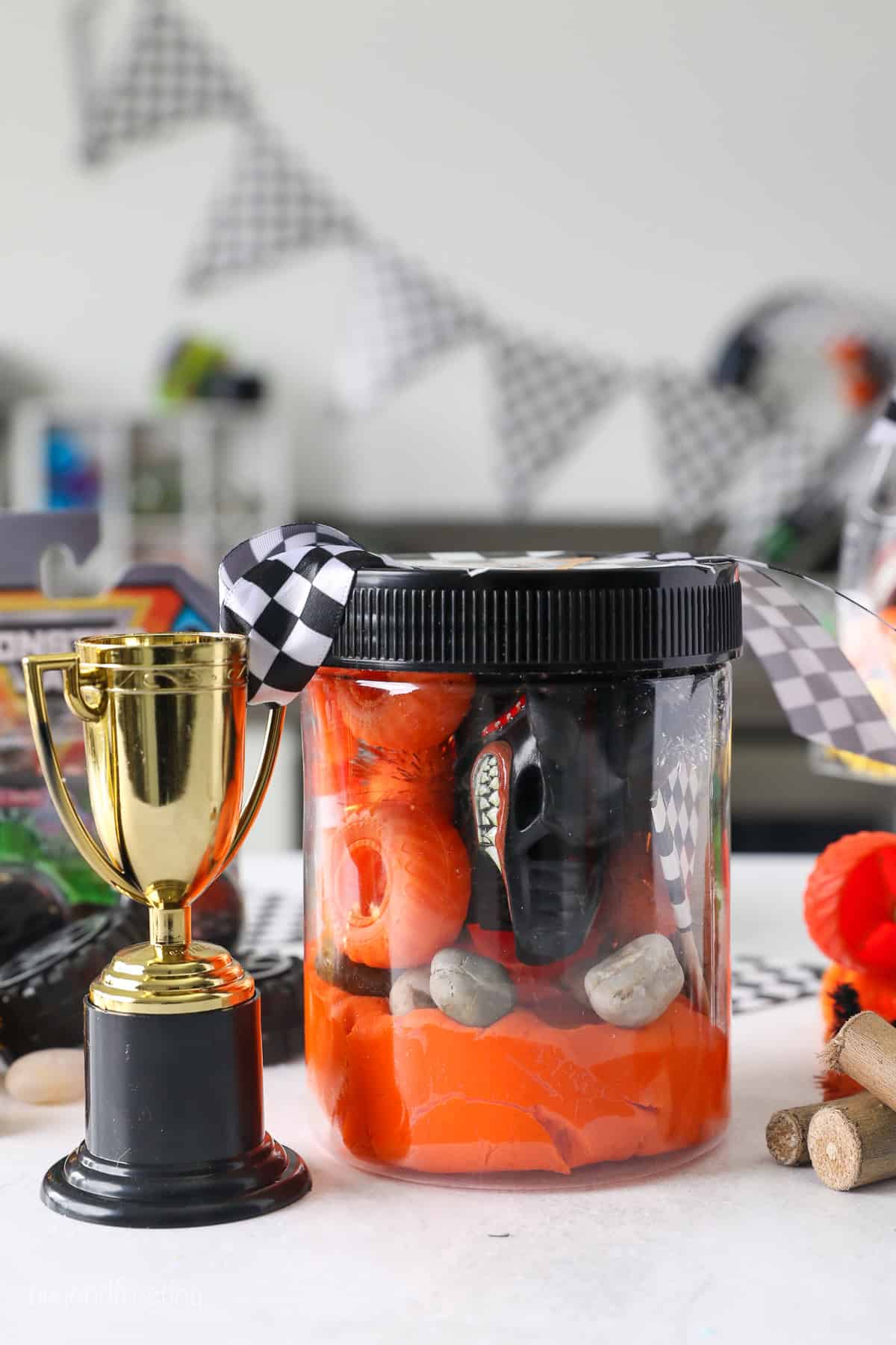 A Monster Jam play dough kit inside a plastic jar next to a mini toy trophy.