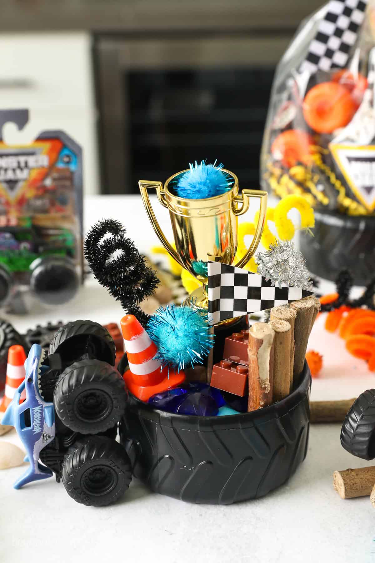 These Monster Jam play dough kits are easy to make with homemade playdough! They make great party favors for a Monster Truck fan's birthday. A tire bowl filled with Monster truck party favors, including mini cones, pompoms, pipe cleaners, mini logs, a mini checkered flag, and a toy trophy.