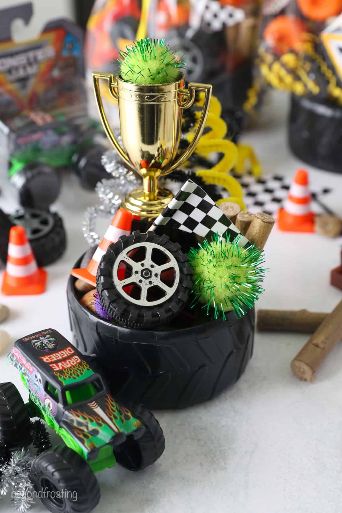 A tire bowl filled with Monster truck party favors, including mini tires, pompoms, a mini checkered flag, and a toy trophy.