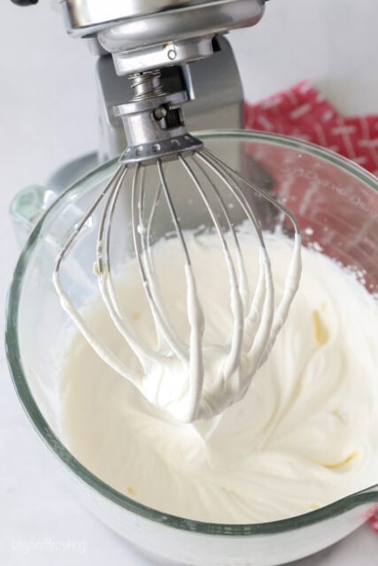 a close up of a whisk in a stand mixer with whipped cream